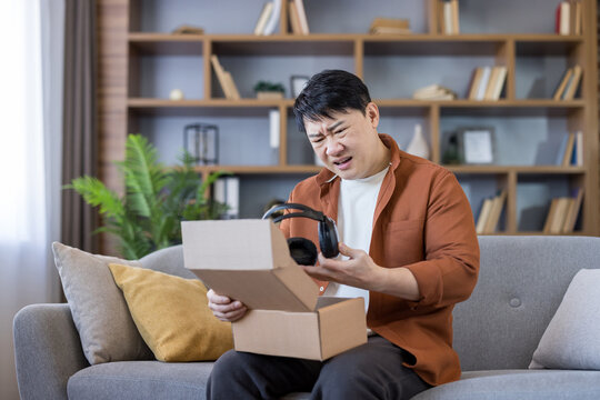 Man unboxing damaged headphones from online purchase sitting sofa