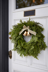 Elegant Christmas holiday wreath with golden bells on white door for festive home decor.