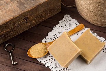 Natural handmade beige soap with wooden spoon of ground herbs and rustic key decor, eco skincare concept.