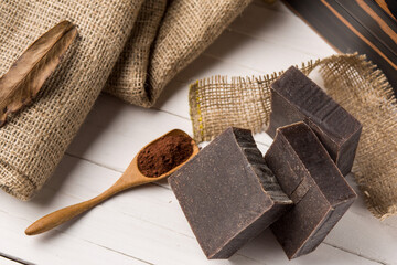 Dark handmade coffee soap bars with wooden spoon of ground coffee, rustic burlap background.