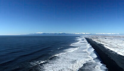 A sweeping vista of a dark sand beach, lapped by waves, stretching towards snow-capped mountains against a vibrant blue sky.