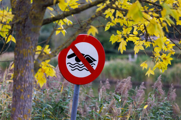 No Swimming sign warns against danger in beautiful autumn lakeside nature setting
