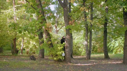 wide view of park wanderer sipping hot tea from mug while strolling under leafy canopy, pausing among green trees and dappled sunlight, slow relaxed movement captured in serene forest setting - Powered by Adobe