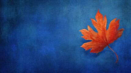 Vibrant orange autumn leaf against a textured, deep blue background creates an inviting, peaceful artistic composition.