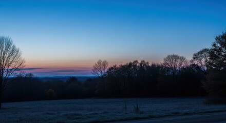 Tranquil autumn sunrise over frosty meadow and silhouetted trees