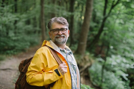Mature man hiking in forest wearing raincoat