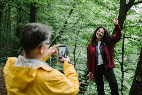 Father photographing happy daughter posing in forest