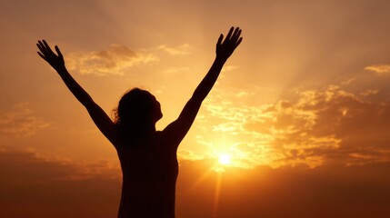 A person stands with arms raised high in joy as the sun sets in the background. The silhouette is outlined by vibrant colors of orange and yellow in the sky, creating a serene moment.