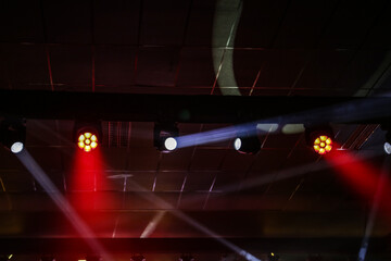 Fachos de holofotes e luzes brancas e vermelhas, em um ambiente de festa. © Angela