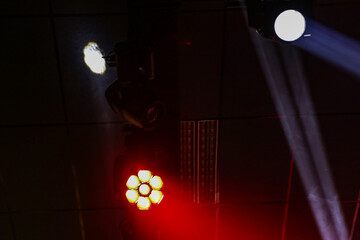 Fachos de holofotes e luzes brancas e vermelhas, em um ambiente de festa. © Angela