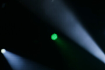 Foto de conjunto de luzes de palco, com fachos de luzes nas cores verde e branca. Desfocadas para fundo. © Angela
