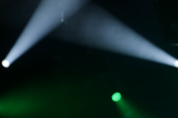 Foto de conjunto de luzes de palco, com fachos de luzes nas cores verde e branca. Desfocadas para fundo. © Angela