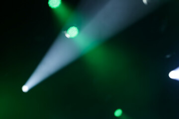 Foto de conjunto de luzes de palco, com fachos de luzes nas cores verde e branca. Desfocadas para fundo. © Angela