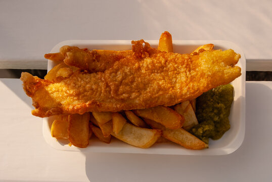 Fish and chips with mushy peas in white Container on white table.