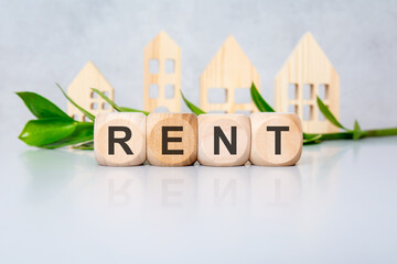Wooden cubes spelling RENT on glossy desk with green leaves and wooden houses in blurred background