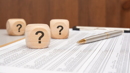 wooden cubes with black question marks on financial spreadsheet with pen and blurred background