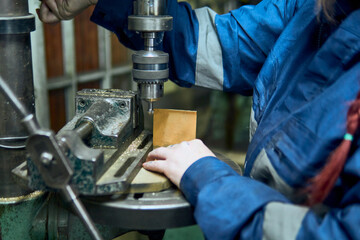 View of a Latina woman's hands working in a workshop, using machinery, a press, tools, bending, drilling, and cleaning. She's wearing a blue suit and doing crafts. Independent, beautiful, and artisan.