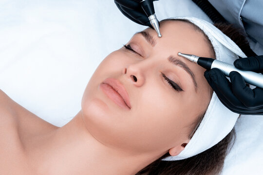 Cosmetology. Beautiful Woman At Spa Clinic Receiving Stimulating Electric Facial Treatment From Therapist. Closeup Of Young Female Face During Microcurrent Therapy