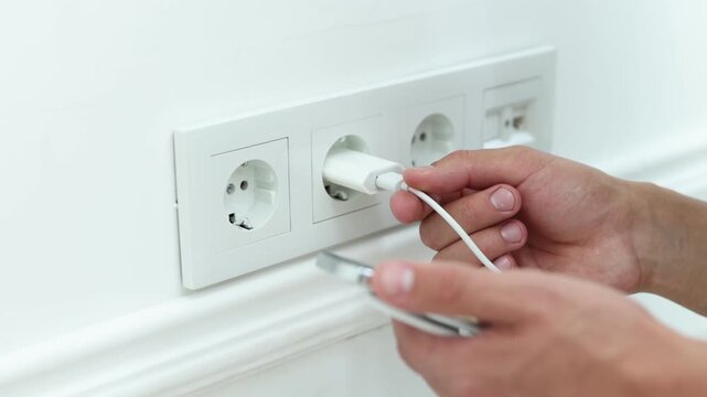 Man plugging smartphone into power socket indoors, closeup