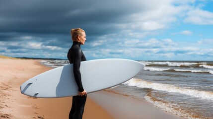 Surfer enjoys the ocean breeze while holding surfboard on sandy beach under cloudy sky