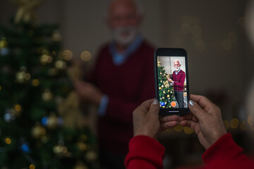 Senior woman filming husband decorating christmas tree on smart phone