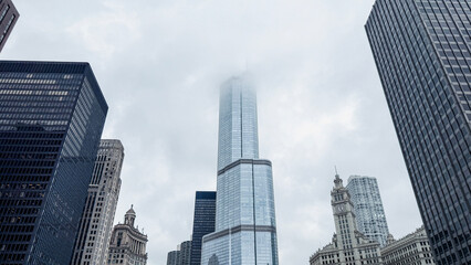 Obraz premium Low angle view of majestic skyscraper Buildings on the Chicago River in Chicago, Illinois. Low clouds envelop the tall buildings reaching to the sky.