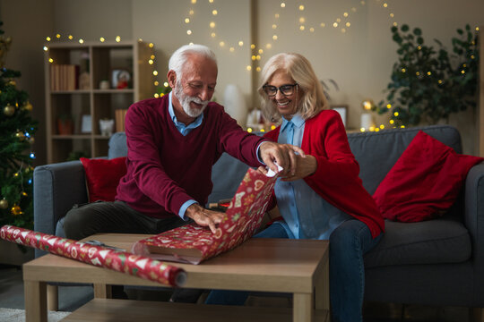 Senior couple wrapping christmas gifts together in living room - Powered by Adobe