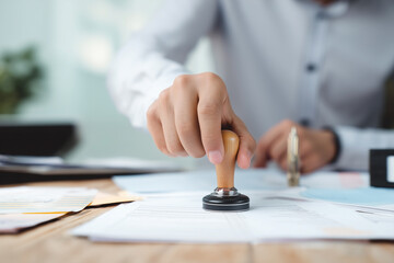 Close up of a hand using a stamp on documents at a desk, representing approval, authentication, or processing paperwork.