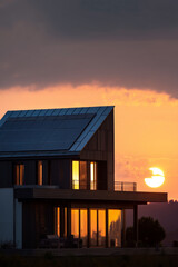 Modern house at sunset with solar panels. Golden light glowing through windows with the sun setting behind the hillside.