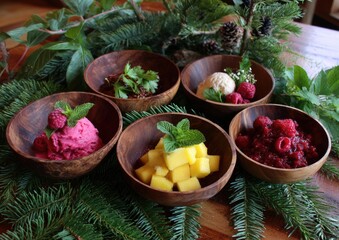Assorted fruit desserts served in rustic wooden bowls, adorned with fresh mint and berries, arranged on a festive table setting.