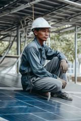 Worker resting on solar panels, wearing a white hard hat, with a focused expression, showcasing clean energy and a contemplative moment.