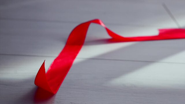 A roll of red satin ribbon lies half-unwound.
A long red ribbon fell to the floor and unraveled.
Holiday ribbon for decorating gifts.