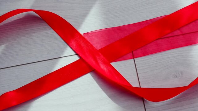 A roll of red satin ribbon lies half-unwound.
A long red ribbon fell to the floor and unraveled.
Holiday ribbon for decorating gifts.