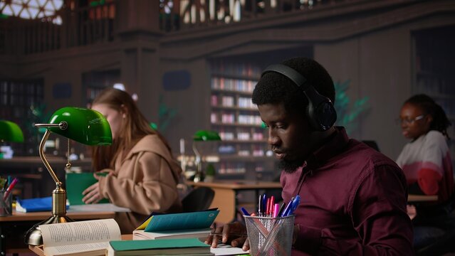 Black guy using study music to help with deep focus for academic success, consulting the campus university database to find reliable sources. Male college student fights for diploma. Camera B.
