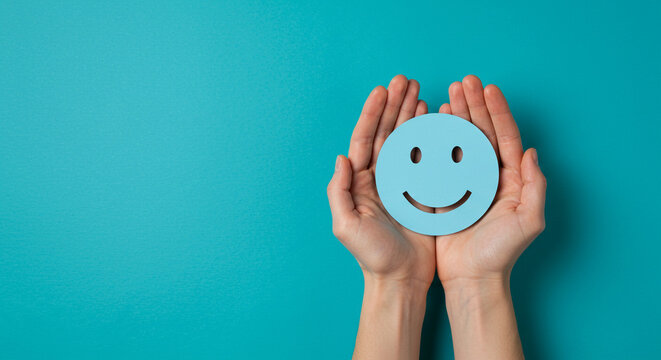 Gentle hands lovingly cradle a vibrant blue happy face emoji, symbolizing joy, excellent customer experience, and positive feedback on a bright teal background.