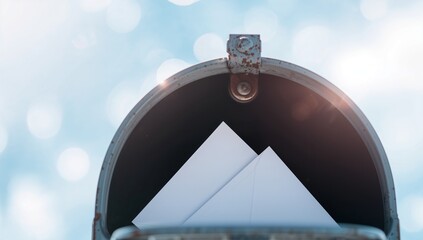 Open mailbox filled with white envelopes under a bright blue sky symbolizing communication, connection, and receiving important news or invitations in the digital age