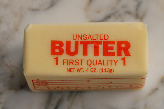 one 4oz stick of Unsalted butter in wrapping on white marble kitchen counter