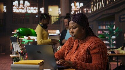 African american positive librarian working in a peaceful public library, offering guidance, mentorship and academic expertise to students. Woman manages educational personalized materials. Camera A.