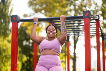 Obraz premium Young smiling woman in pink sportswear hanging on a crossbar
