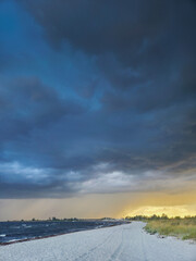 Obraz premium Dramatic coastal scene with stormy skies above a tranquil beach at sunset
