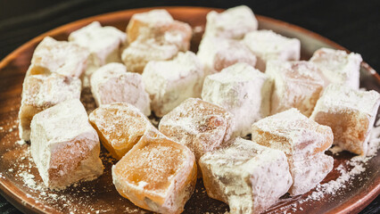 A plate of Turkish delight sweets ready to be served. The soft, square candies are dusted with powdered sugar, arranged neatly on a simple plate for an elegant presentation.