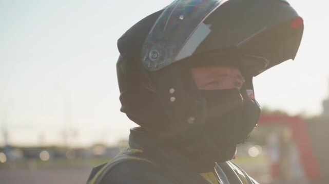 Close up side view of rider lifting helmet visor as passenger climbs behind, sunlight glow creating cinematic atmosphere with blur background highlighting leather gear and anticipation of motorcycle