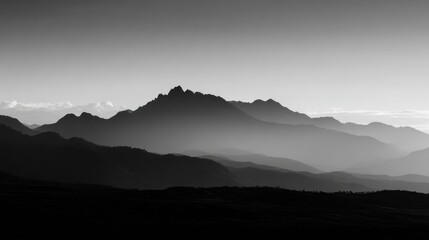 Monochromatic landscape showcasing layered mountain silhouettes against a pale sky, suggesting either dawn or dusk.  The mountains' forms are distinct yet softened by atmospheric perspective