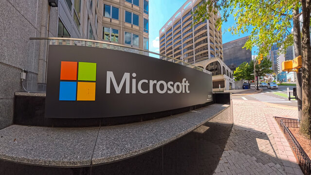 Corporate Microsoft sign in front of glass office buildings. Clear blue sky and tree reflections.