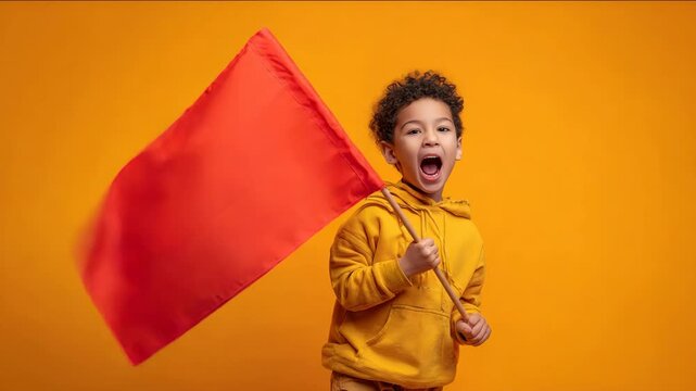 A young boy shouts while waving a red flag against a vibrant orange background.