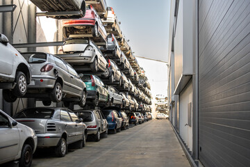 Stacked cars in scrapyard with multiple vehicles lined up on shelves. The scene shows rows of cars...