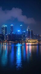 Fototapeta premium Night Cityscape Reflections on Water Dark Blue Night Sky with Clouds and Illuminated Buildings Urban Glow City Lights Mirroring in Calm Water at Night