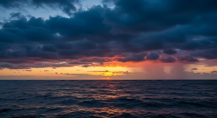 Obraz premium Dramatic sunset over ocean with vibrant colors and dark clouds
