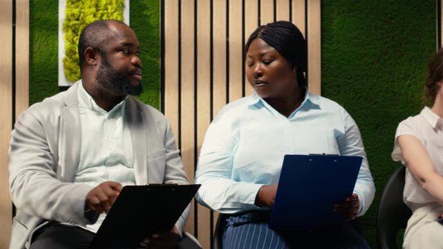 Confident job applicants sitting in the hallway before hiring interview, reviewing their CVs and preparing for employment questions with HR recruiters during a talent acquisition meeting. Camera B.