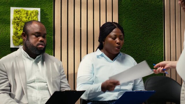 Female secretary handing documents and CVs to job applicants in lineup on the corridor, filling in important information and preparing for the career opportunity. Workplace support. Camera B.